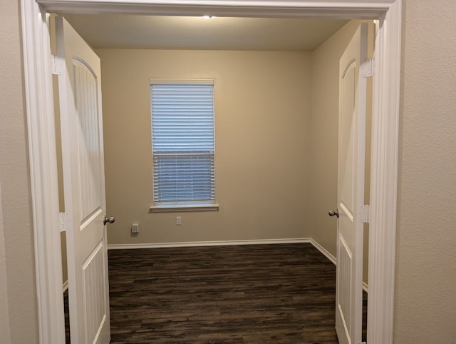 empty room with dark wood-type flooring and baseboards