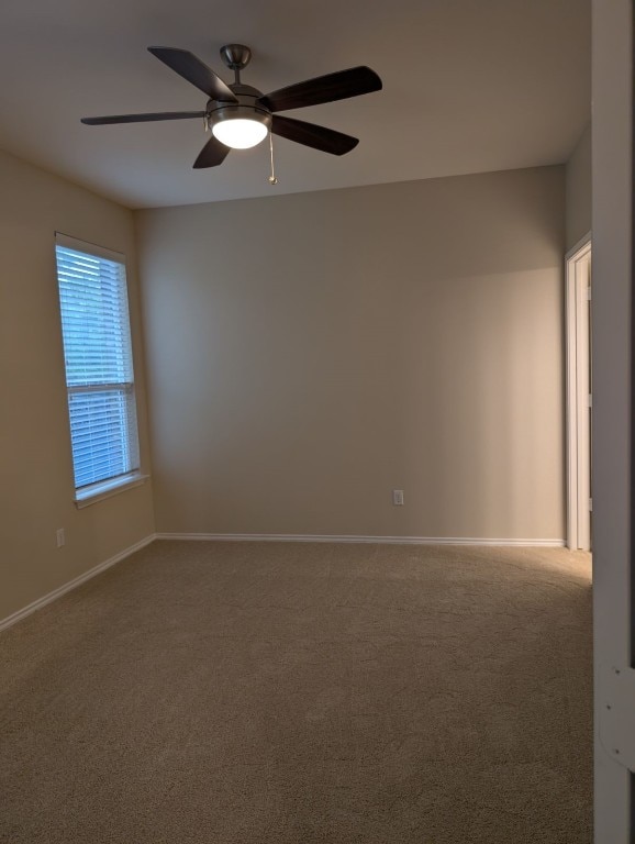 carpeted spare room featuring a ceiling fan and baseboards