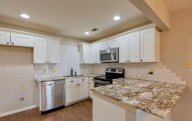 kitchen with visible vents, a peninsula, stainless steel appliances, light wood-type flooring, and a sink