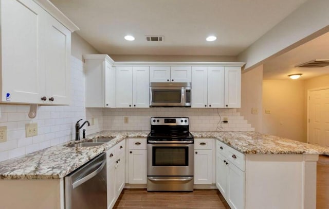 kitchen featuring stainless steel appliances, a peninsula, wood finished floors, a sink, and visible vents