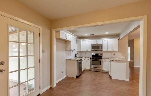 kitchen featuring stainless steel appliances, tasteful backsplash, light wood-style floors, white cabinets, and a sink