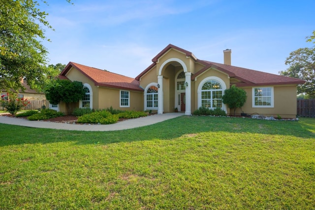 view of front of property with fence, a chimney, a front lawn, and stucco siding