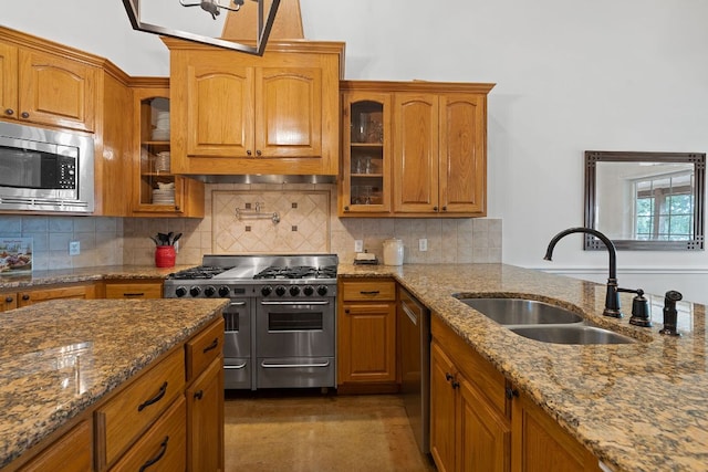 kitchen with brown cabinets, stainless steel appliances, tasteful backsplash, stone countertops, and a sink