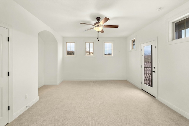 empty room featuring baseboards, arched walkways, a ceiling fan, and light colored carpet