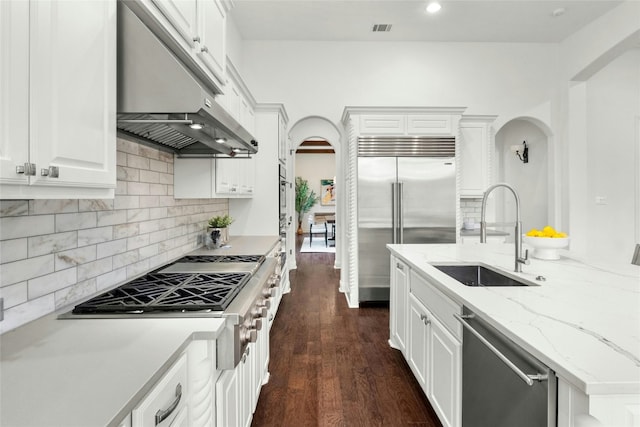 kitchen with arched walkways, under cabinet range hood, stainless steel appliances, a sink, and visible vents