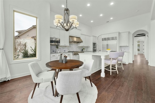 dining room featuring arched walkways, a chandelier, dark wood-style flooring, and recessed lighting