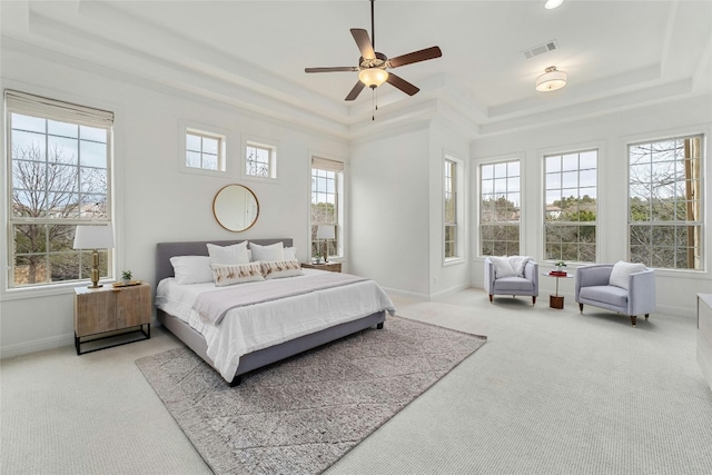 carpeted bedroom with a tray ceiling, multiple windows, visible vents, and baseboards