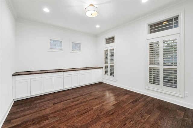 empty room with dark wood-type flooring, crown molding, and baseboards