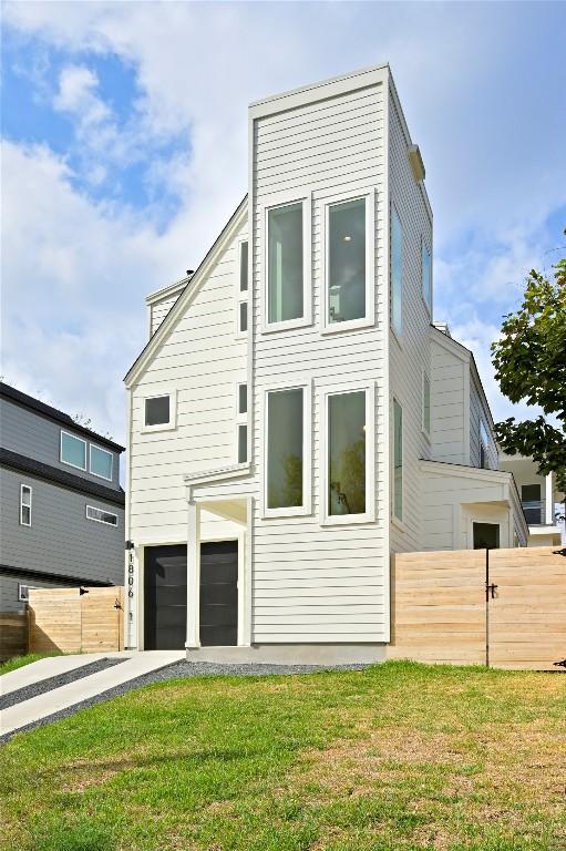 rear view of property with a garage, fence, driveway, and a lawn