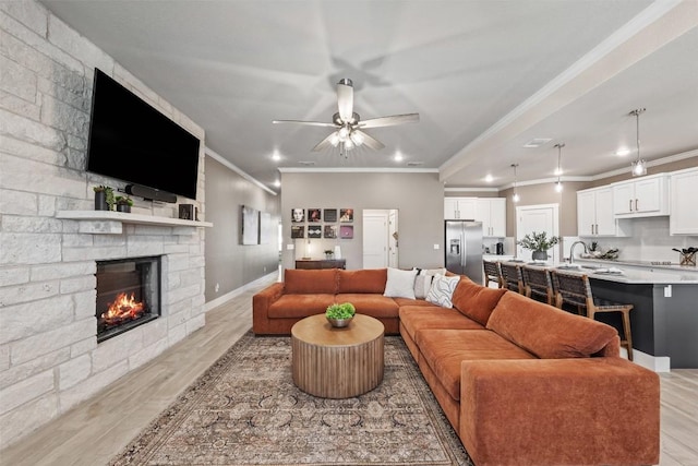 living room with light wood-type flooring, ornamental molding, and a stone fireplace