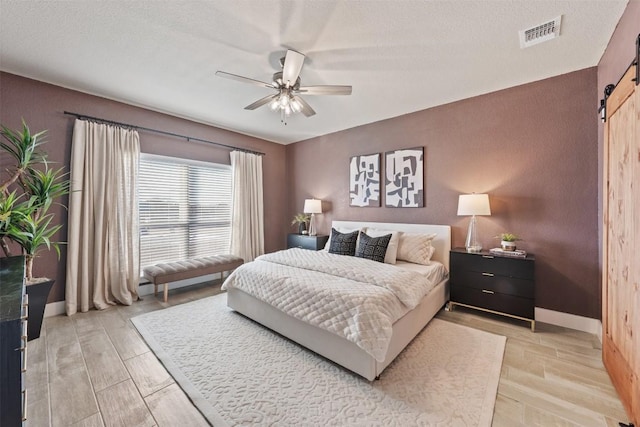 bedroom featuring light wood-style floors, visible vents, baseboards, and a barn door