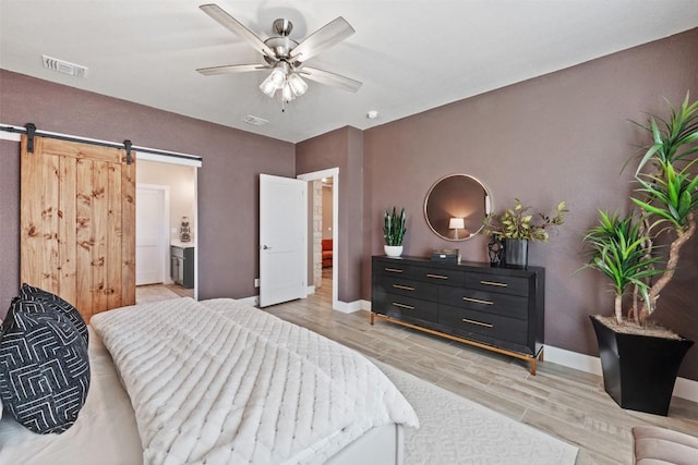 bedroom featuring visible vents, a barn door, a ceiling fan, light wood-type flooring, and baseboards