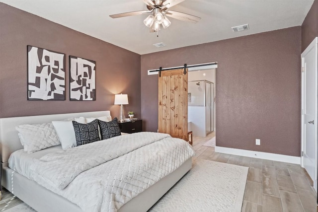 bedroom featuring visible vents, a barn door, a ceiling fan, wood finished floors, and baseboards