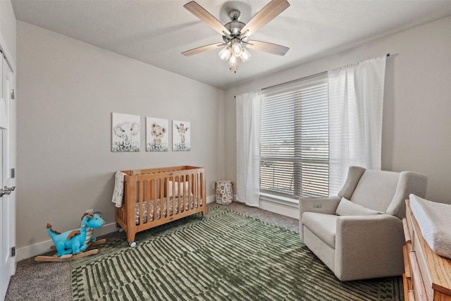 carpeted bedroom featuring a crib, a ceiling fan, and baseboards