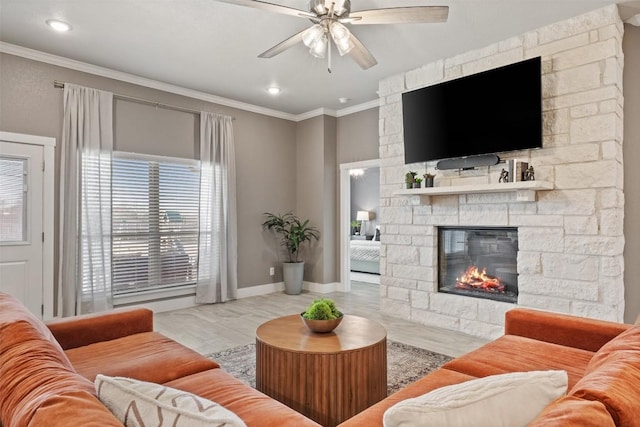 living area with baseboards, ornamental molding, a ceiling fan, and a stone fireplace