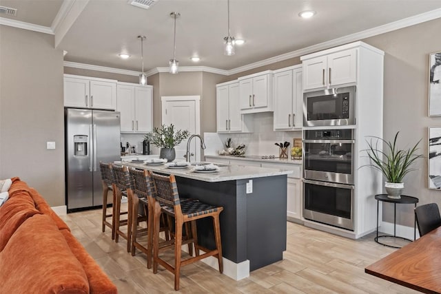 7701 Soapstone Ct, Temple, TX 76502 - kitchen with appliances with stainless steel finishes, a breakfast bar area, light wood-type flooring, crown molding, and white cabinetry