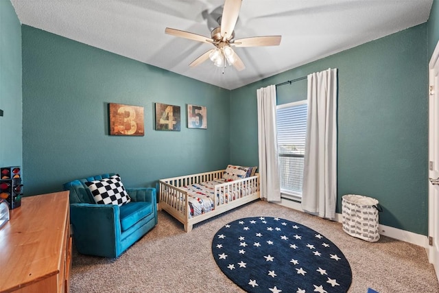 carpeted bedroom with a ceiling fan, a nursery area, and baseboards