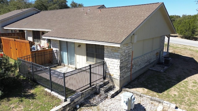 rear view of house with a shingled roof, stone siding, fence, central AC, and brick siding