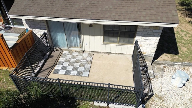 exterior space featuring a shingled roof, stone siding, and fence