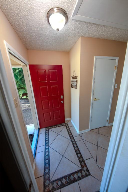 foyer entrance with a textured ceiling, light tile patterned flooring, and baseboards