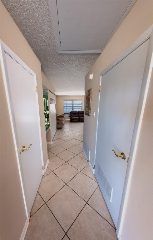 hall featuring a textured ceiling, light tile patterned floors, and attic access