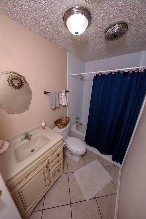 bathroom with a textured ceiling, tile patterned flooring, toilet, vanity, and shower / bath combo with shower curtain