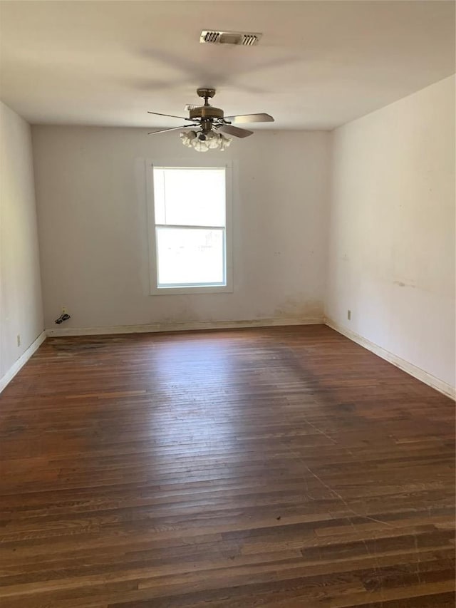 spare room featuring ceiling fan, visible vents, dark wood finished floors, and baseboards