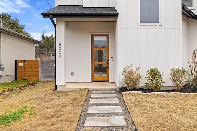 entrance to property with fence, board and batten siding, and roof with shingles