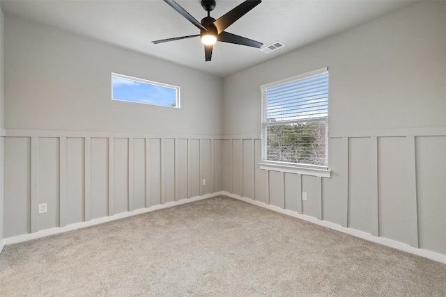 carpeted empty room featuring a ceiling fan, wainscoting, visible vents, and a decorative wall