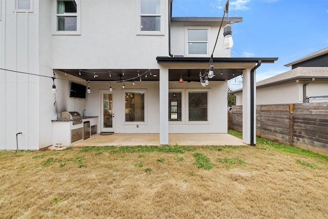 rear view of property featuring area for grilling, fence, a lawn, stucco siding, and a patio area