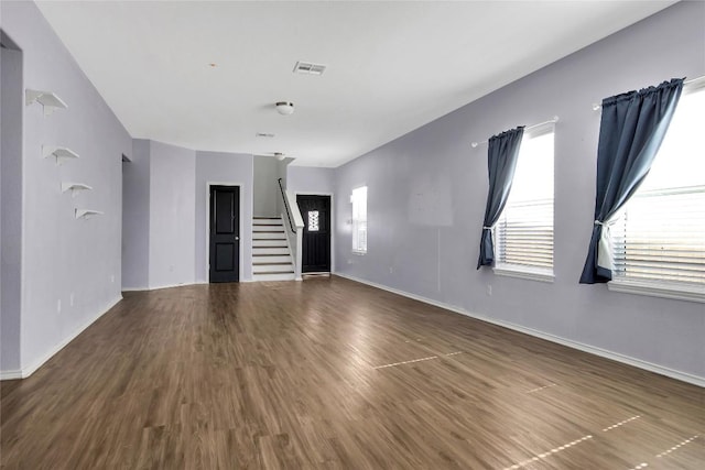 unfurnished living room with stairs, wood finished floors, visible vents, and baseboards