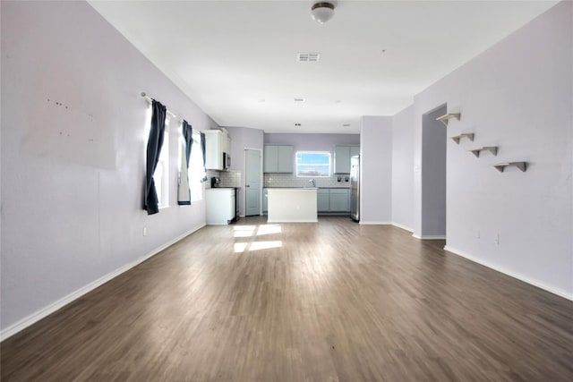 unfurnished living room with a sink, wood finished floors, visible vents, and baseboards