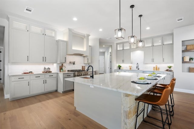 kitchen with light wood finished floors, visible vents, a large island, premium range hood, and a sink