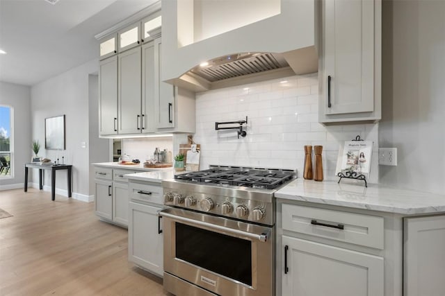 kitchen with premium range hood, light wood-style floors, tasteful backsplash, stainless steel range, and glass insert cabinets