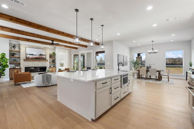 kitchen featuring a large fireplace, a sink, visible vents, and light wood-style floors