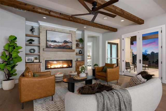 living area featuring ceiling fan, a fireplace, wood finished floors, visible vents, and beamed ceiling