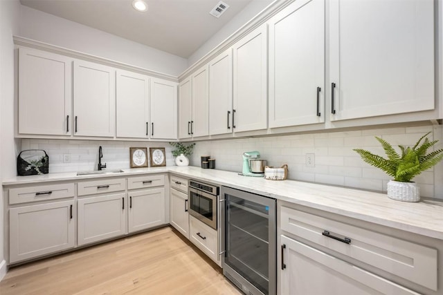 kitchen with visible vents, wine cooler, stainless steel microwave, a sink, and backsplash