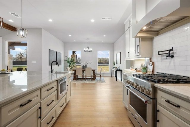 kitchen with a sink, visible vents, wall chimney range hood, high end stainless steel range, and light wood-type flooring