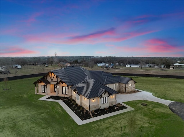 back of house at dusk with a standing seam roof, stucco siding, metal roof, and a yard