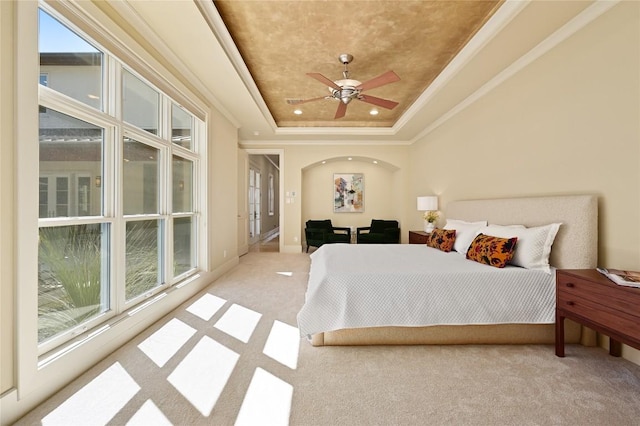 bedroom with arched walkways, a raised ceiling, ceiling fan, ornamental molding, and carpet flooring