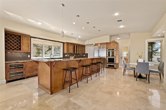 kitchen with appliances with stainless steel finishes, a kitchen breakfast bar, brown cabinets, and light stone counters