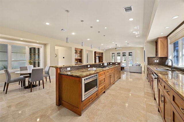 kitchen with a sink, visible vents, open floor plan, appliances with stainless steel finishes, and brown cabinetry