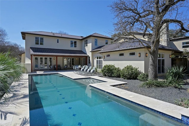 back of house featuring metal roof, french doors, stucco siding, a standing seam roof, and a patio area