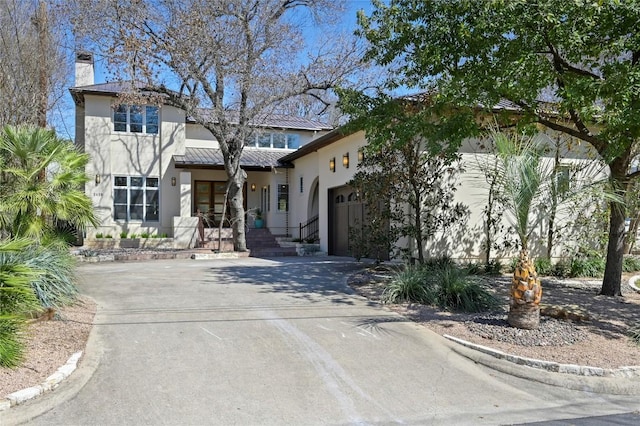 view of front of house with stucco siding, a standing seam roof, metal roof, a garage, and driveway