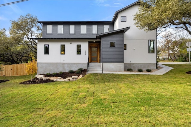 contemporary house featuring entry steps, fence, and a front lawn