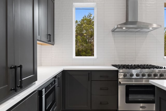 kitchen featuring stainless steel stove, light countertops, decorative backsplash, built in microwave, and wall chimney exhaust hood