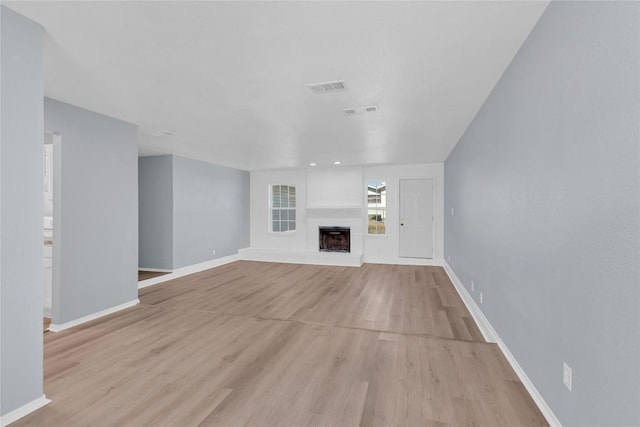 unfurnished living room with light wood finished floors, baseboards, visible vents, and a fireplace with raised hearth