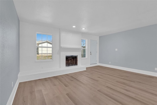 unfurnished living room with recessed lighting, a brick fireplace, light wood-style flooring, and baseboards