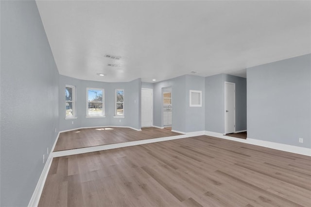 unfurnished living room with baseboards, visible vents, and wood finished floors