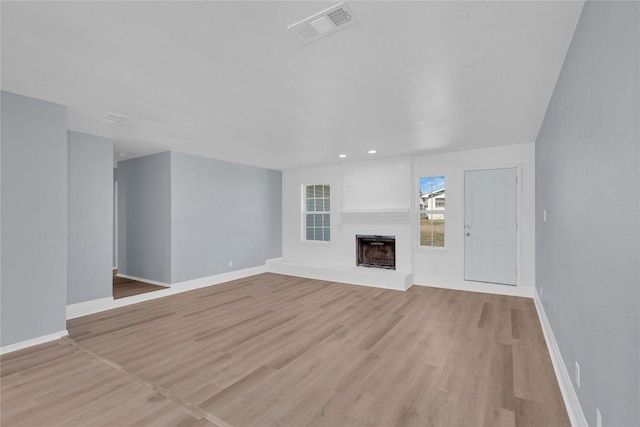 unfurnished living room featuring light wood-type flooring, visible vents, a fireplace with raised hearth, and baseboards